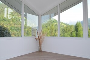 Ein Zimmer mit großen Fenstern, Holzboden und einer Vase mit Trockenpflanzen.