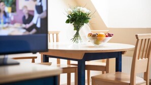 A dining area with a round table, chairs, a vase with flowers, and a bowl of fruit. - Donauauen Apartments (Schwechat)
