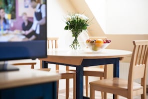 Ruokailutila, jossa on pyöreä pöytä, tuoleja, maljakko kukkineen ja kulho täynnä hedelmiä.