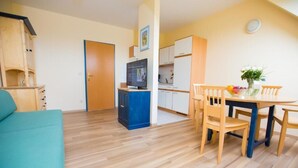 A compact living space with a kitchenette, a dining area with wooden chairs, a sofa, and a television. - Donauauen Apartments (Schwechat)