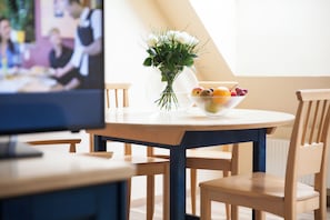 Un comedor con una mesa redonda, sillas, un florero con flores y un bol de fruta.