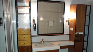 A bathroom with a wooden vanity, a large mirror, and a shower enclosure. - Donauauen Apartments (Schwechat)