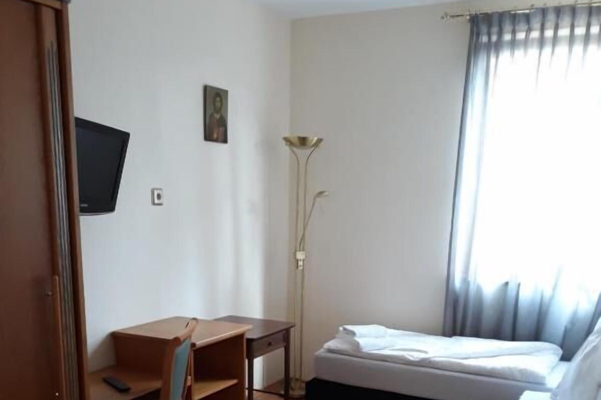 Una habitación con cama, escritorio, silla, televisor y lámpara.