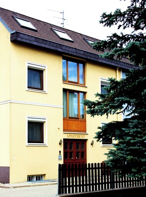 Un edificio de dos pisos con fachada amarilla, puerta roja y un letrero que dice 'APARTMENT'.