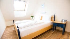 A single bed with a wooden frame, a bedside table with a drawer, a small bedside lamp, and a window with blinds. - Donauauen Apartments (Schwechat)