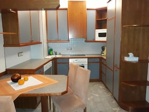 Cocina compacta con armarios de madera, microondas, estufa y comedor con mesa y sillas.