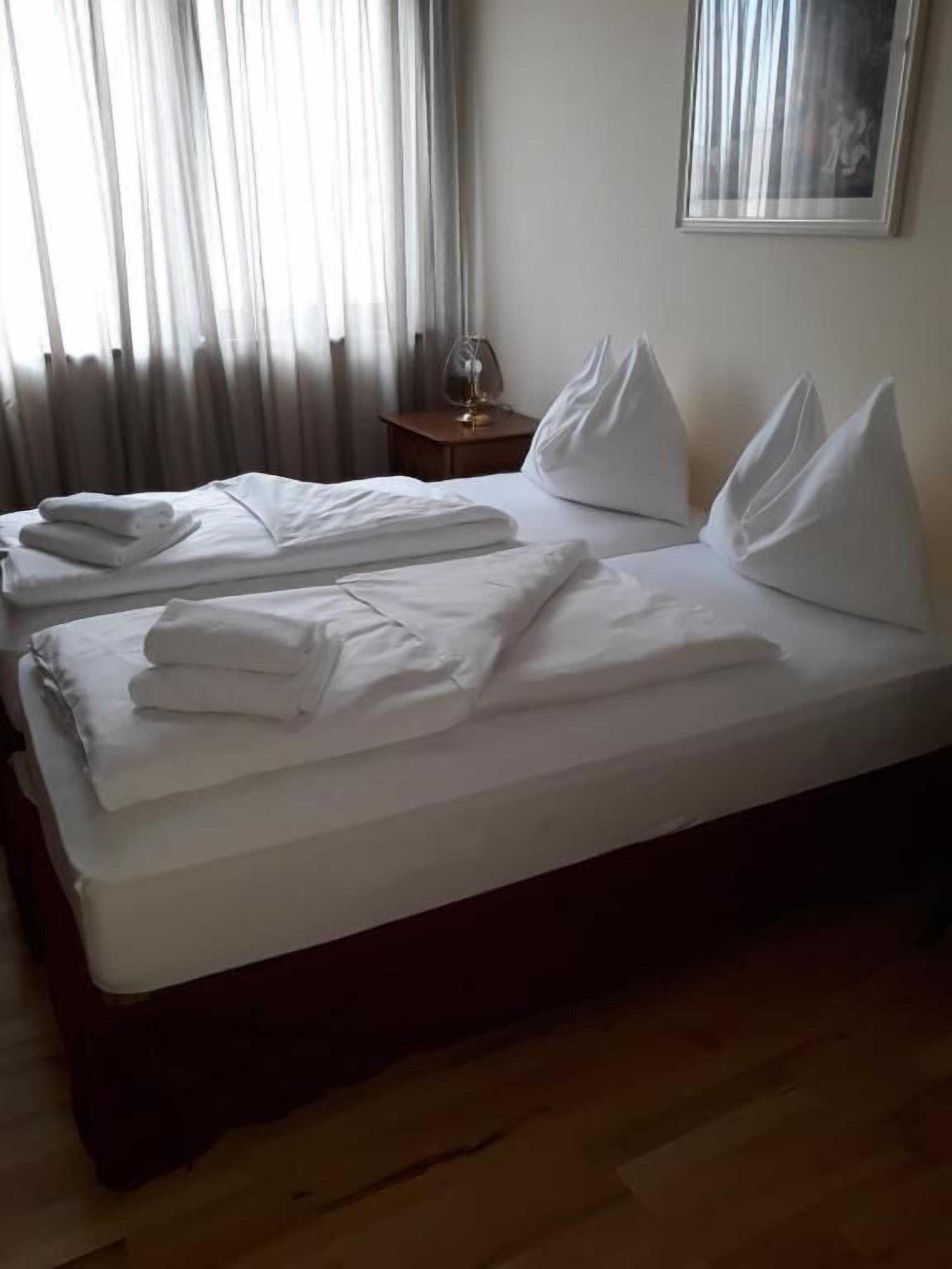 Ein Hotelzimmer mit einem ordentlich bezogenen Bett, einem Nachttisch mit Lampe und einem gerahmten Bild an der Wand.