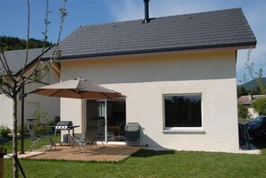 A single-story house with a patio area, a barbecue grill, and a large window. - Anya - 3*** - AUTRANS-MEAUDRE IN VERCORS (AUTRANS-MEAUDRE EN VERCORS)