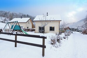 Una casa amb un teulat cobert de neu, un tobogan i un cotxe aparcat a la calçada.