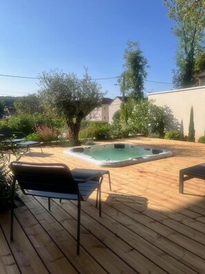 Eine Holzterrasse mit Liegestühlen, einem Whirlpool und einem Pool.