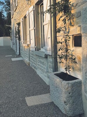 Un bâtiment en pierre avec une allée en gravier et un bac à fleurs contenant une plante.