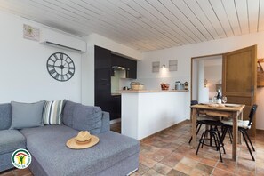 A modern living space with a grey sofa, a dining table with chairs, a kitchen area, and a wooden door. - In the Countryside - PORCIEU AMBLAGNIEU (PORCIEU AMBLAGNIEU)