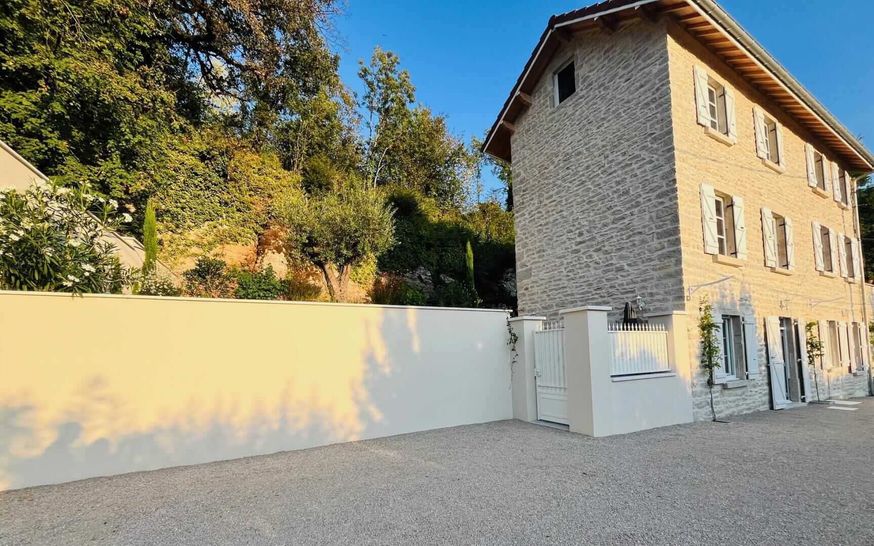 Un bâtiment en pierre avec un mur blanc et une entrée fermée par un portail.
