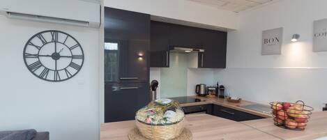 A modern kitchen with a wooden countertop, a large clock, and a basket of fruits.