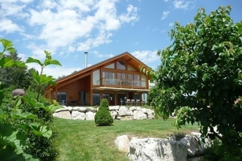 A two-story wooden house with a stone foundation, large windows, and a well-maintained lawn.