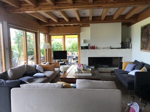 A spacious living room with a fireplace, comfortable seating, and large windows. - The Wooden Case - PONSONNAS (PONSONNAS)