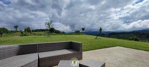 Eine Sitzgruppe aus Korbmöbeln mit Blick auf ein saftiges Grasfeld und ferne Berge.