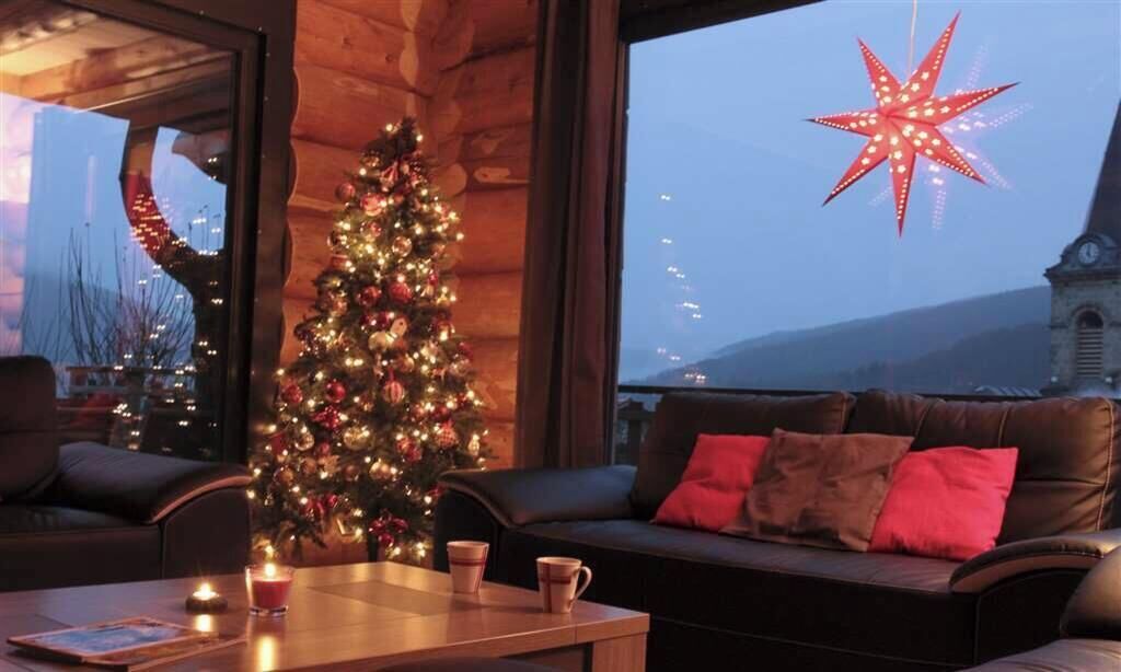Um quarto acolhedor com árvore de Natal, sofá de couro e uma janela grande com vista para um prédio e montanhas.