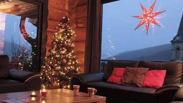 Um quarto acolhedor com árvore de Natal, sofá de couro e uma janela grande com vista para um prédio e montanhas.
