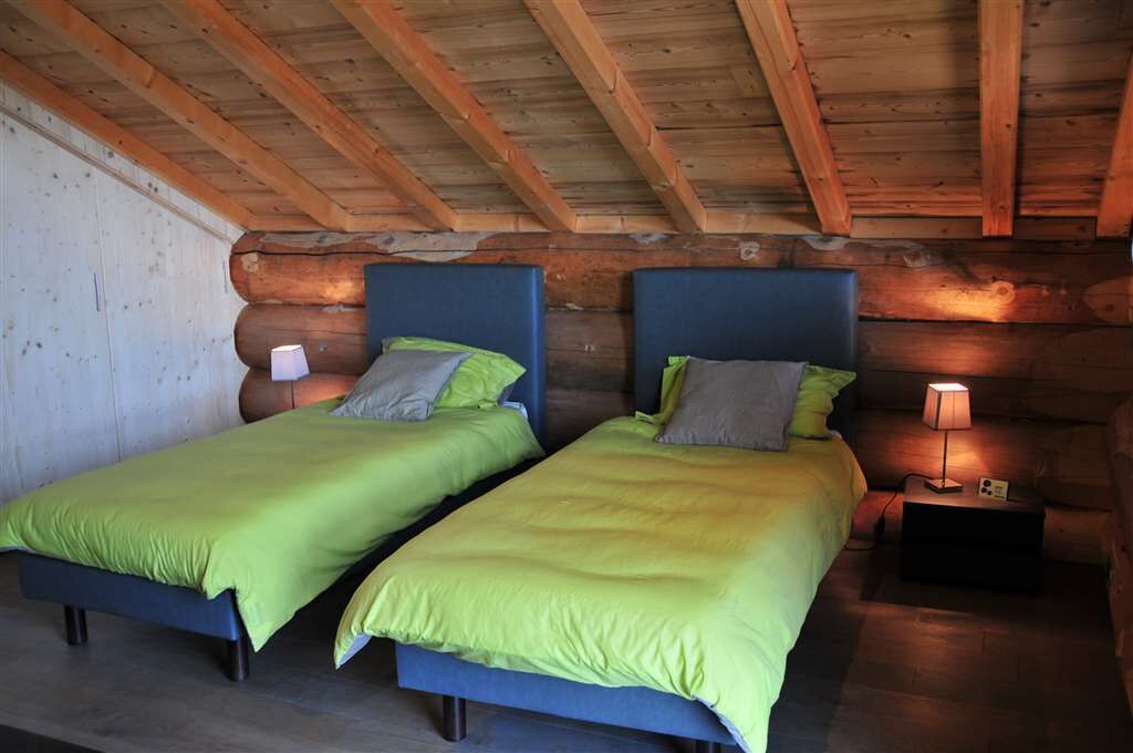 A log cabin room with two beds, each with a headboard and bedside lamp.