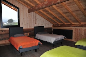 Quarto com três camas, uma janela grande e teto de madeira.