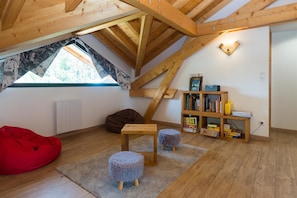 Ein Schlafzimmer im Spitzboden mit geneigter Decke, einem Fenster mit Blick, einem Bücherregal, einem roten Sitzsack und einem kleinen Tisch.