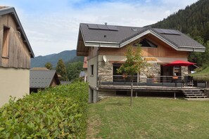 Ein modernes, zweistöckiges Haus mit Steinaußenfassade, einem Balkon mit Sitzgelegenheit und Blick auf die umliegenden Berge.