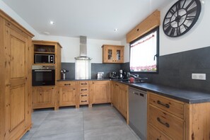 A modern kitchen with wooden cabinets, a stainless steel range hood, a microwave, and a large wall clock. - From L'Arguille - LE HAUT-BREDA (LE HAUT-BREDA)