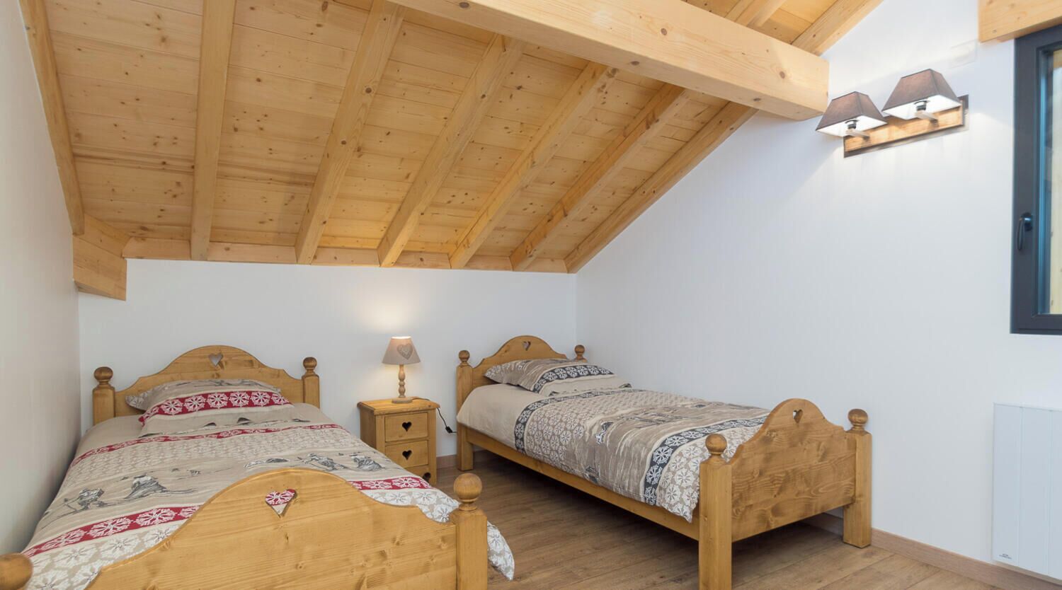 Ein Schlafzimmer mit zwei Holzbetten, einem Nachttisch mit Lampe und einer schrägen Decke.