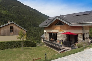 A mountain lodge with a stone facade, a wooden deck, and a red umbrella. - From L'Arguille - LE HAUT-BREDA (LE HAUT-BREDA)