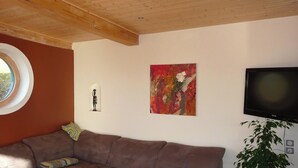 En stue med en brun sofa, et rundt vindue, et billede og et fjernsyn.