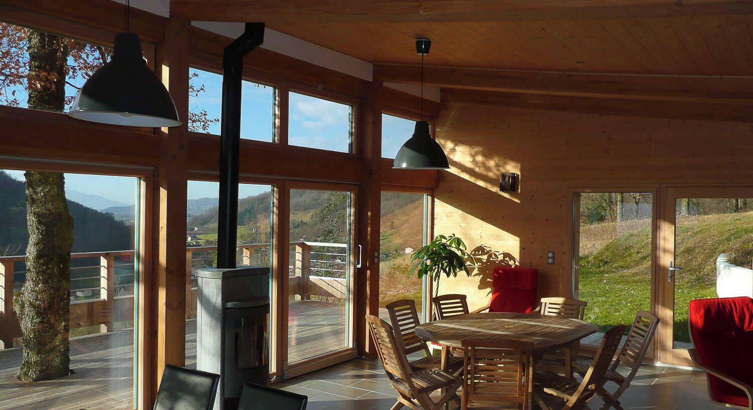 A wooden interior with a table and chairs, large windows, and a view of the outdoors.