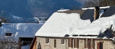 Un bâtiment en pierre dont le toit est recouvert de neige, entouré d’une clôture en bois et situé sur un terrain également recouvert de neige.