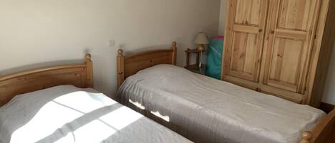 A bedroom with two wooden beds, a wardrobe, and a wall-mounted mirror.