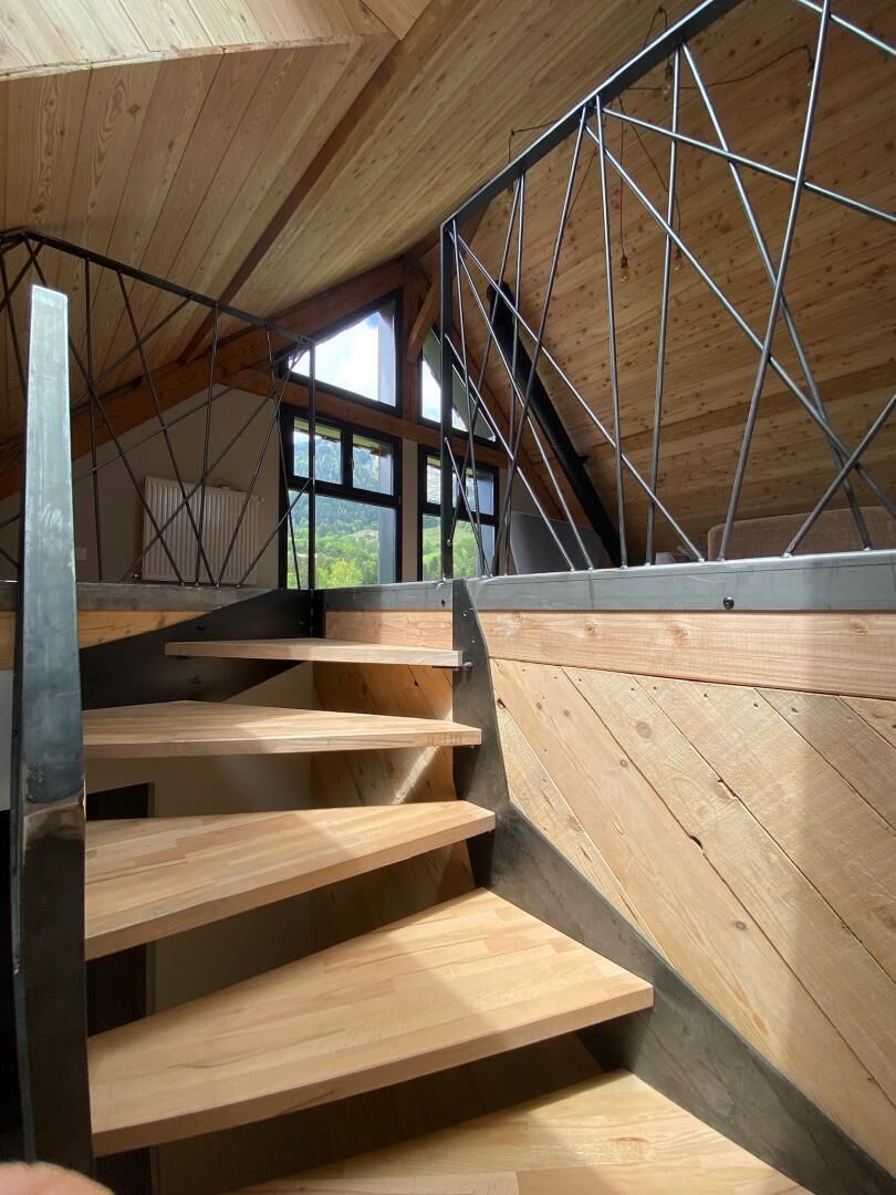 A wooden staircase with metal railings leading to a lofted area with large windows.