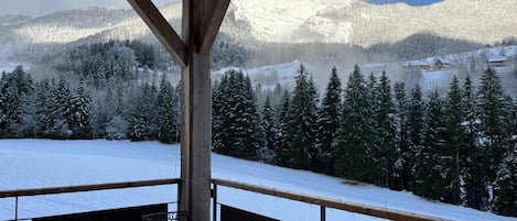 Une terrasse en bois offrant une vue sur des montagnes et des arbres enneigés.