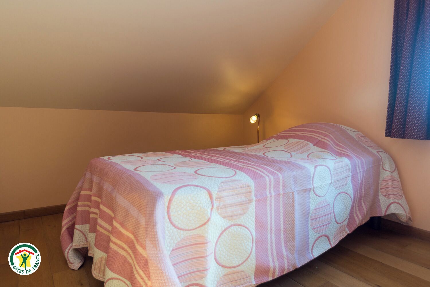 Une petite chambre avec un lit simple, un plafond en pente et une lampe de chevet.