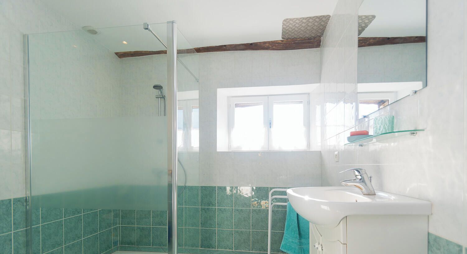 Un baño con cabina de ducha de vidrio, un lavabo blanco y una ventana que proporciona luz natural.