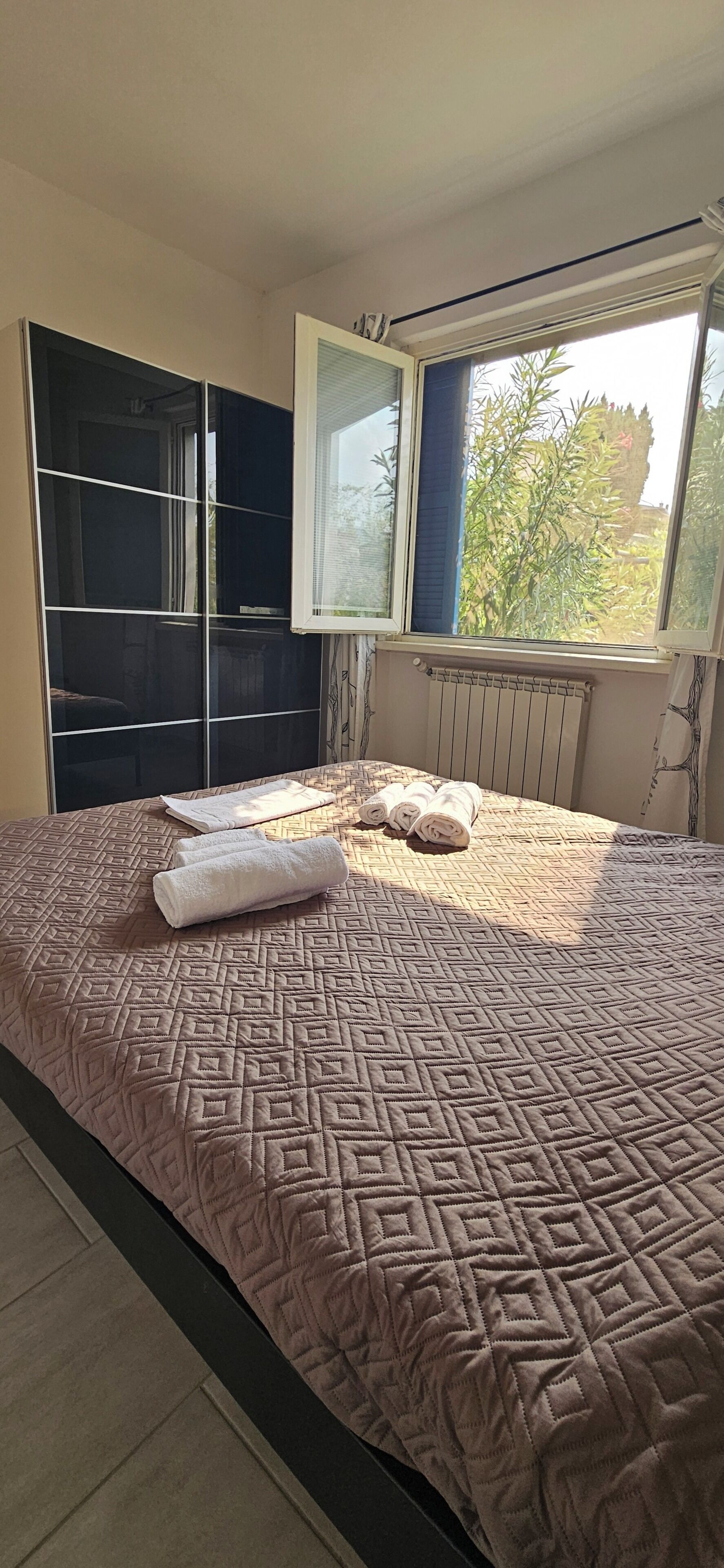Un dormitorio con cama, radiador, ventana y armario.
