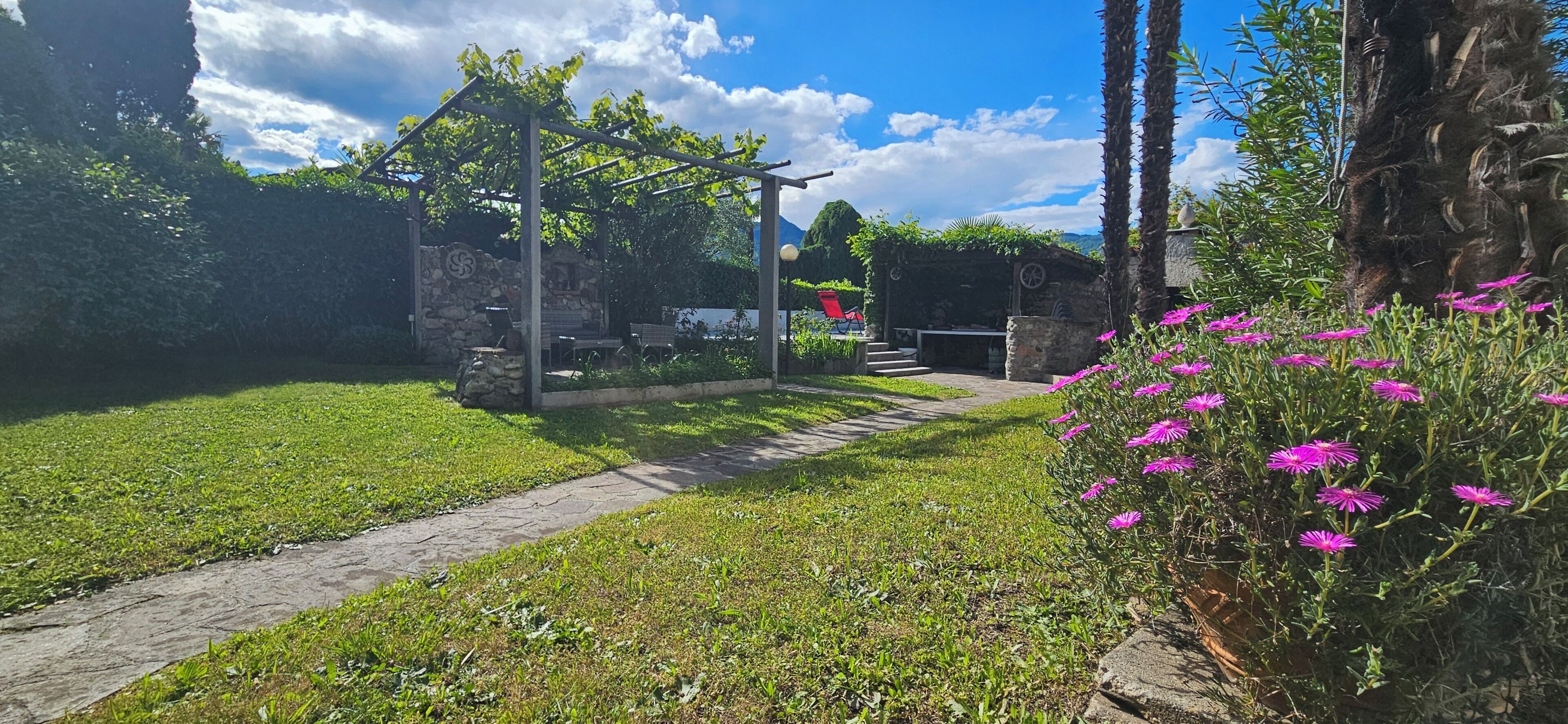 Un jardín con un pérgola, una estructura de piedra y un sendero.