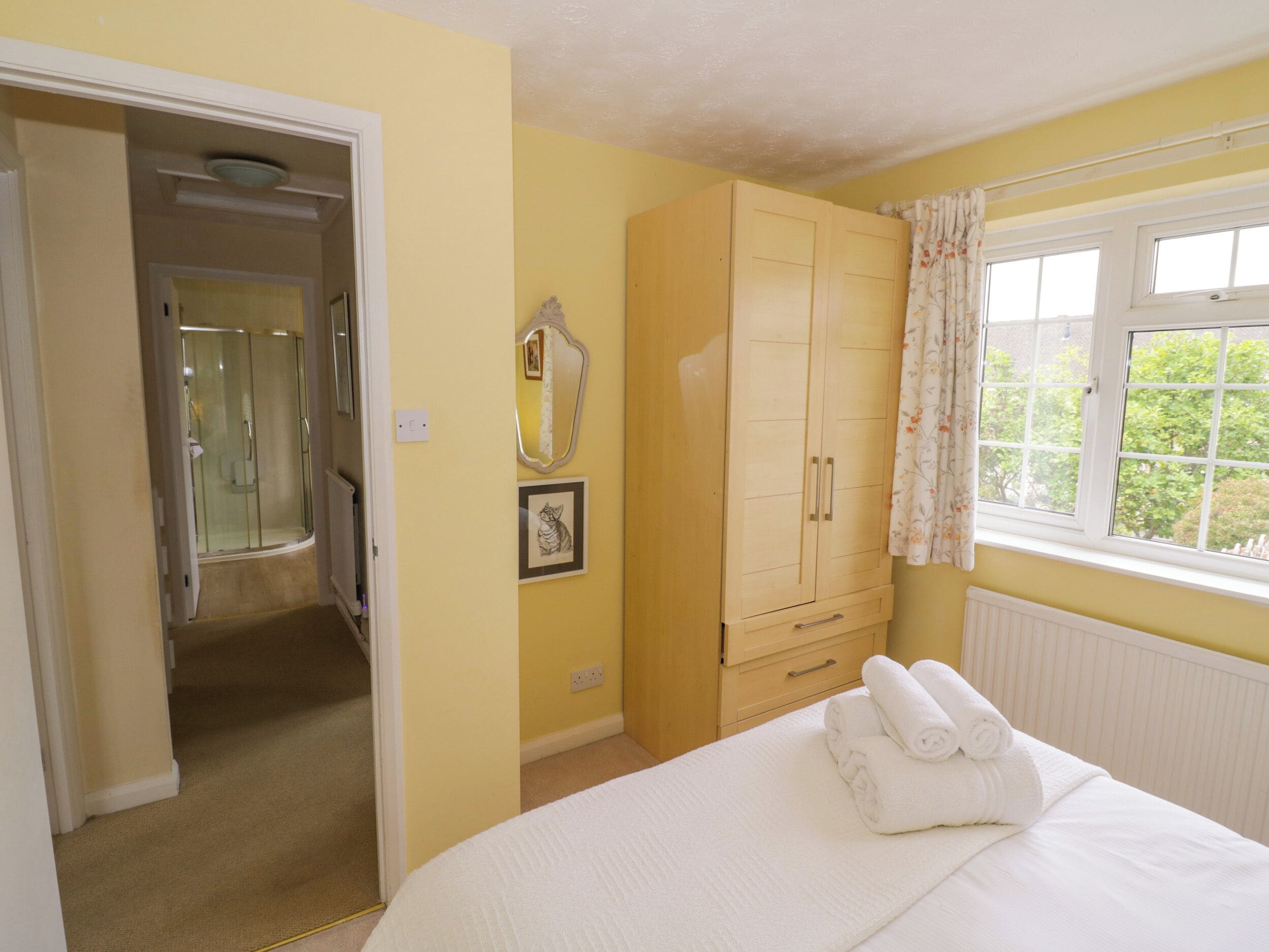 A bedroom with a bed, a wardrobe, a window with curtains, and a bathroom with a shower.
