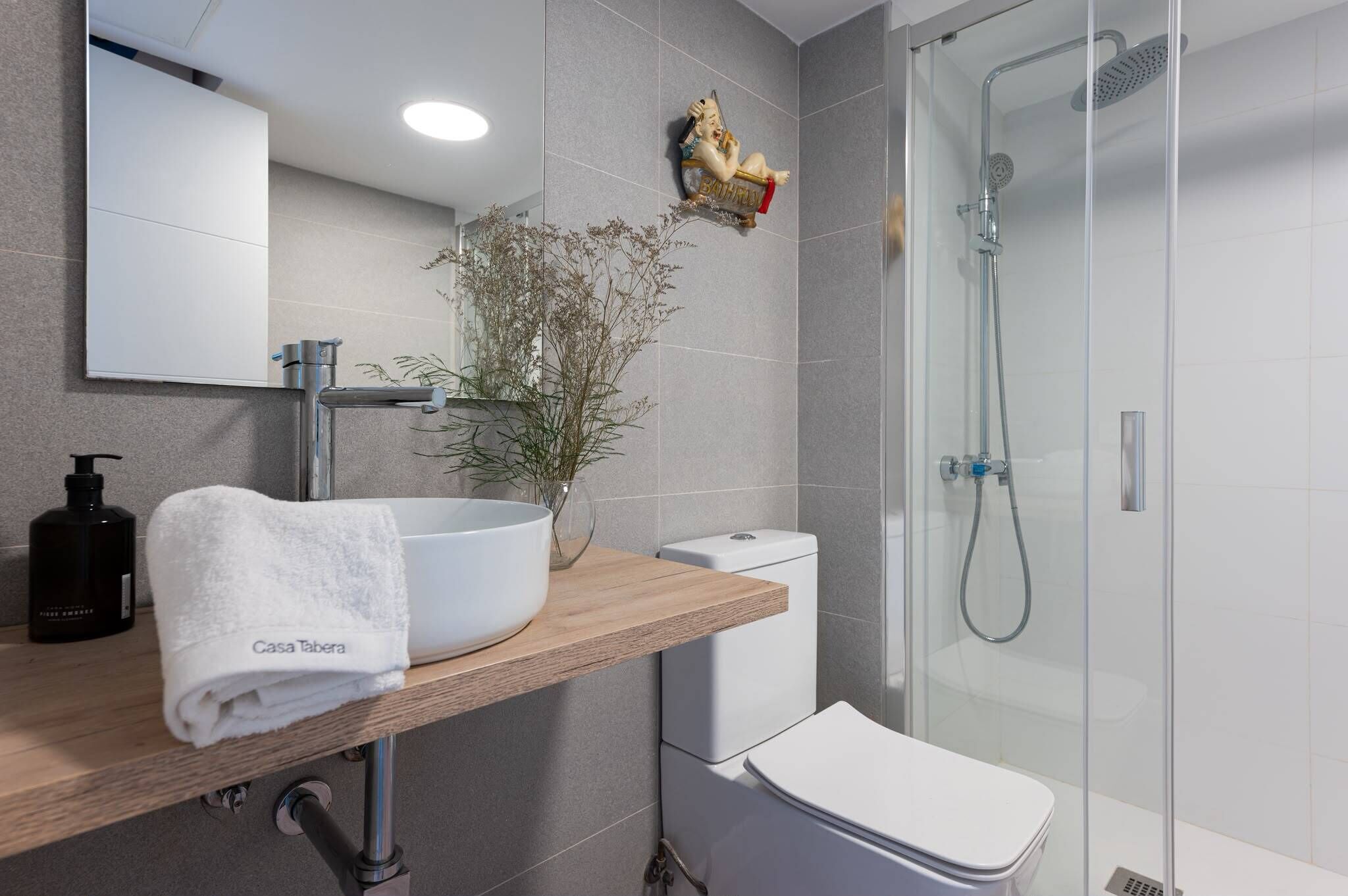 Ein modernes Badezimmer mit einem weißen Waschbecken, einer Duschkabine aus Glas und einem dekorativen Wandbild.