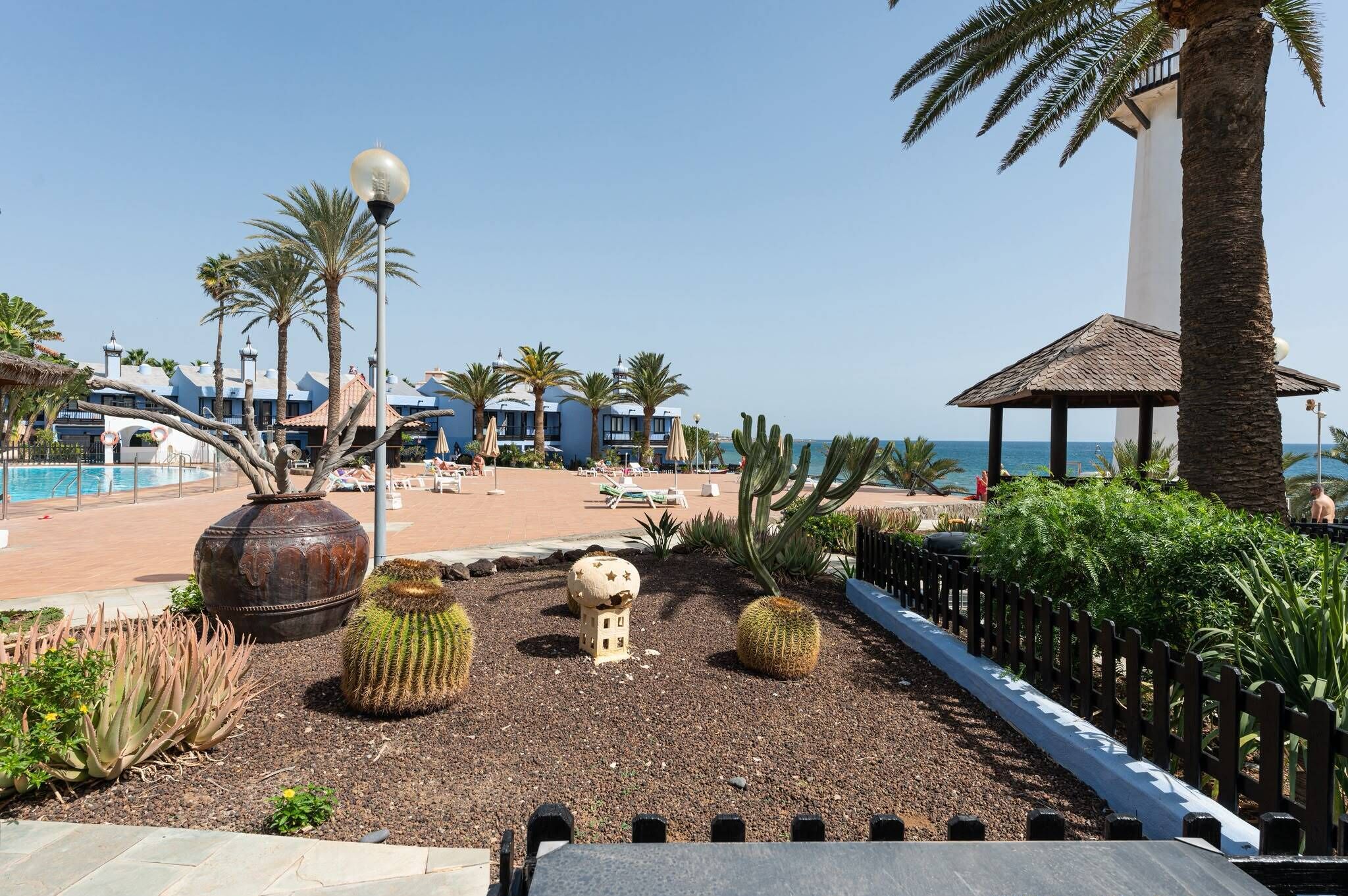 Zona de piscina en un resort con palmeras, un pabellón y vista al océano.