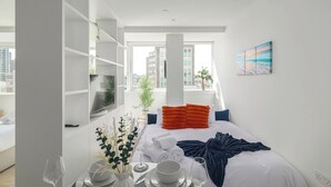 Ein modernes Hotelzimmer mit einem Bett, einer Essecke mit Tisch für zwei Personen, einem Fernseher und einem großen Fenster mit Blick auf die Stadt.