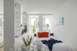 Ett modernt hotellrum med en säng, en matplats med ett bord för två personer, en TV och ett stort fönster med utsikt över staden.