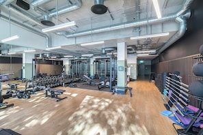 A gym with exercise equipment, wooden flooring, and a high ceiling with ductwork. - Wembley Studio | Cinema, Gym & Workspace (England)