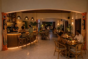 Un restaurante con zona de bar, mobiliario de mimbre e iluminación cálida.