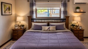 Een slaapkamer met een bed, twee nachtkastjes, een raam met gordijnen, een wandairconditioner en een ingelijste foto aan de muur.
