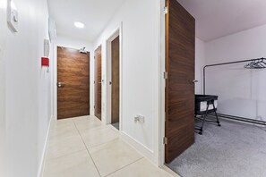 Un pasillo con puerta de madera, pared blanca y suelo de baldosas.