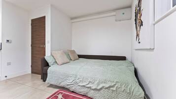 A bedroom with a bed, a door, a wall-mounted air conditioner, and a window with a curtain.